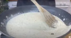 Stirring creamy risotto in a black pan with a wooden spoon on a stove.